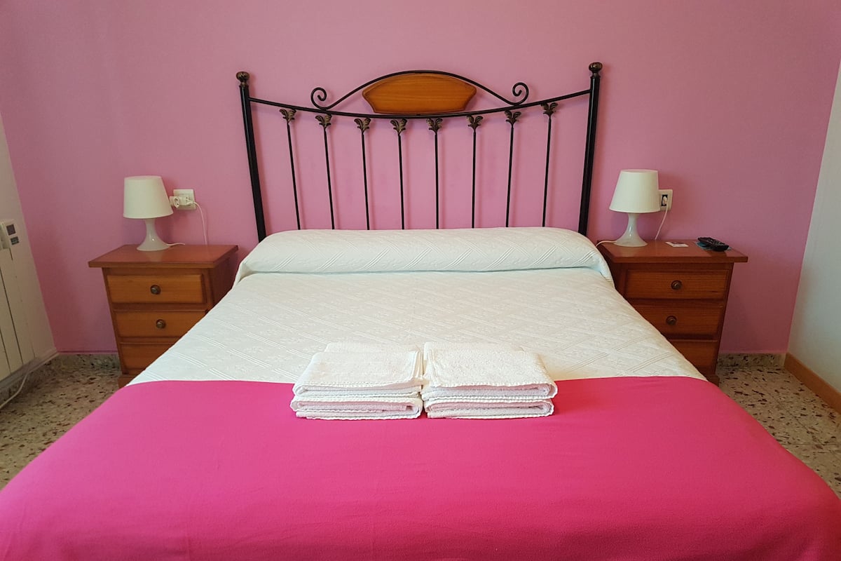 Un lit recouvert d’une couvre-lit rose, avec deux serviettes blanches pliées posées sur le dessus.