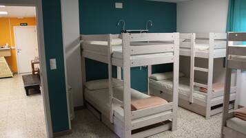 Camas literas en una habitación con paredes azul verdoso y una puerta blanca con la leyenda "SALIDA".