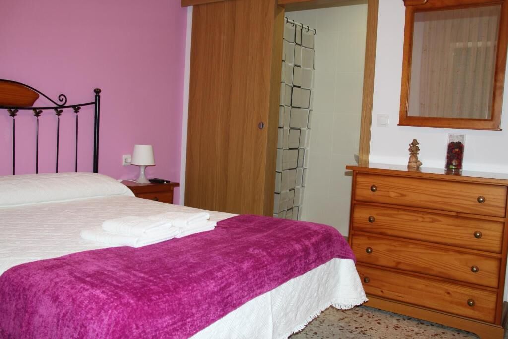 Ein Schlafzimmer mit einem Bett, einer Holzkommode, einem Nachttisch und einem Spiegel.