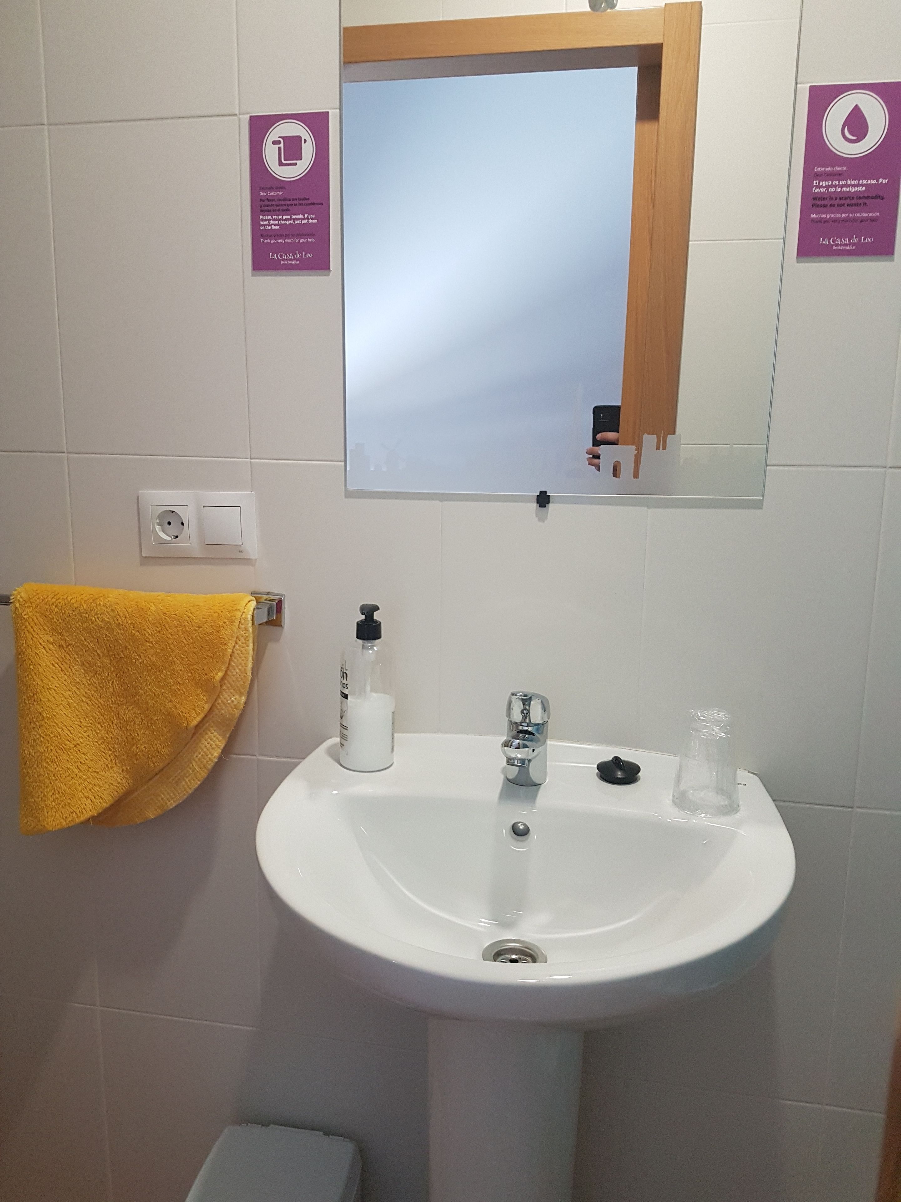 Un baño con lavamanos blanco, un espejo, una toalla amarilla, un dispensador de jabón y un grifo.