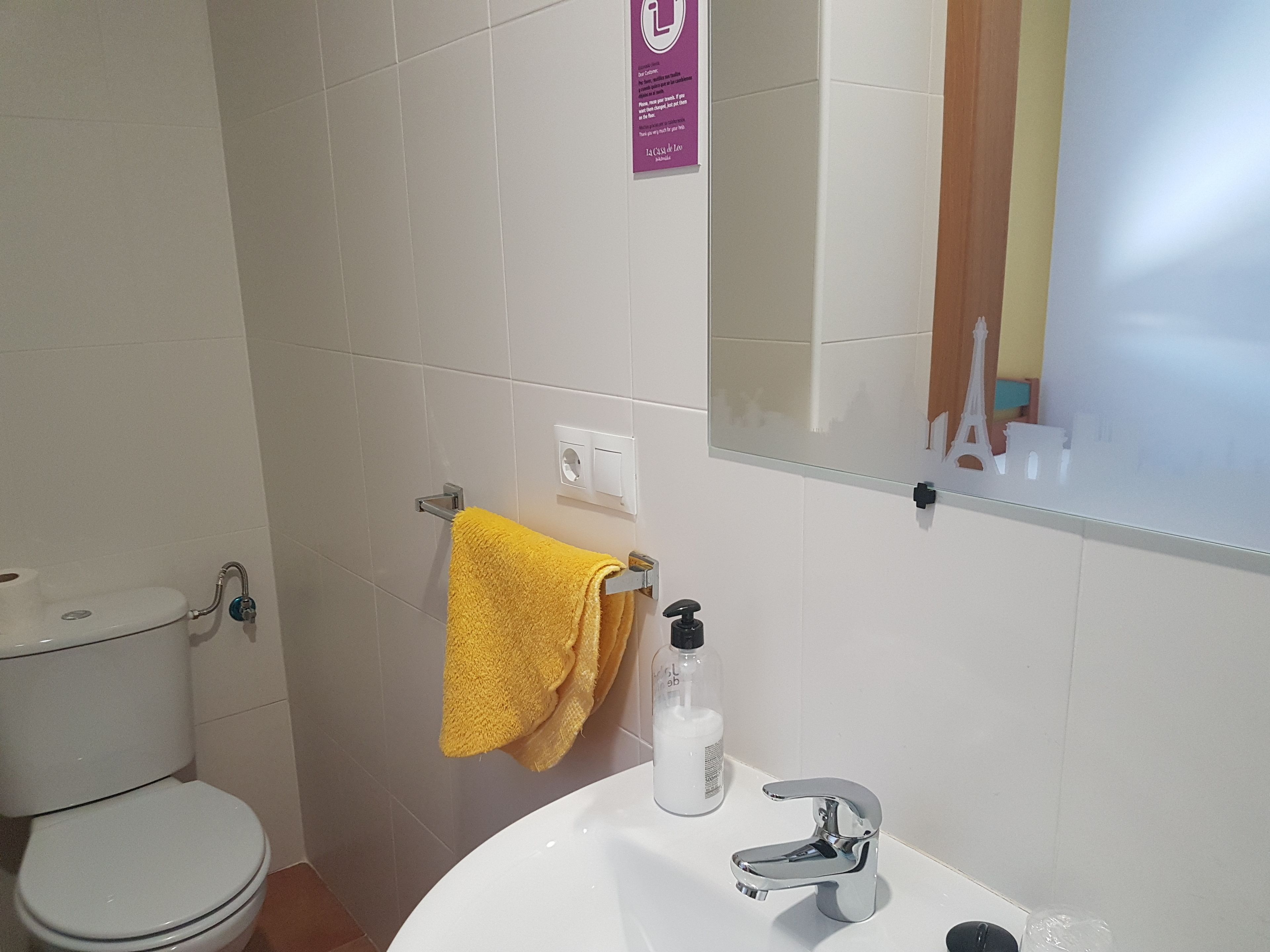 A bathroom with a white toilet, a sink with a chrome faucet, and a yellow towel hanging on a rack.
