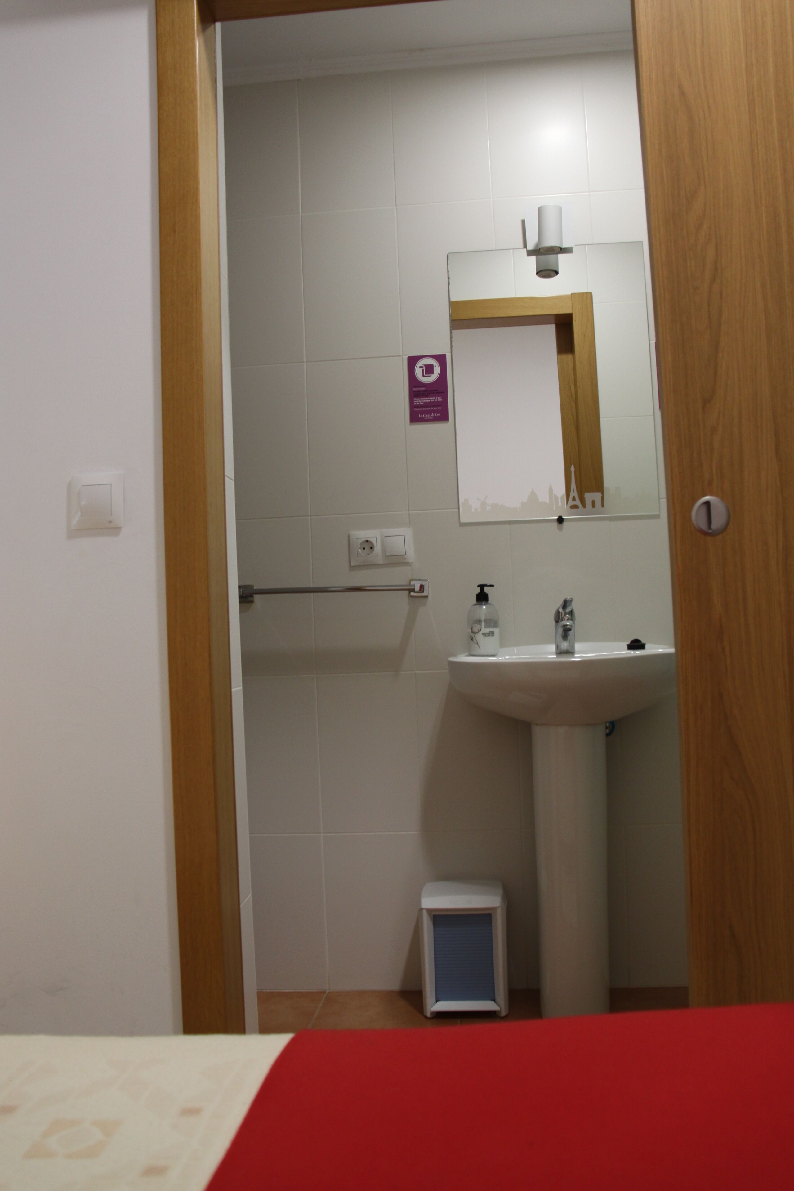 A bathroom with a white sink, mirror, and a small trash bin.
