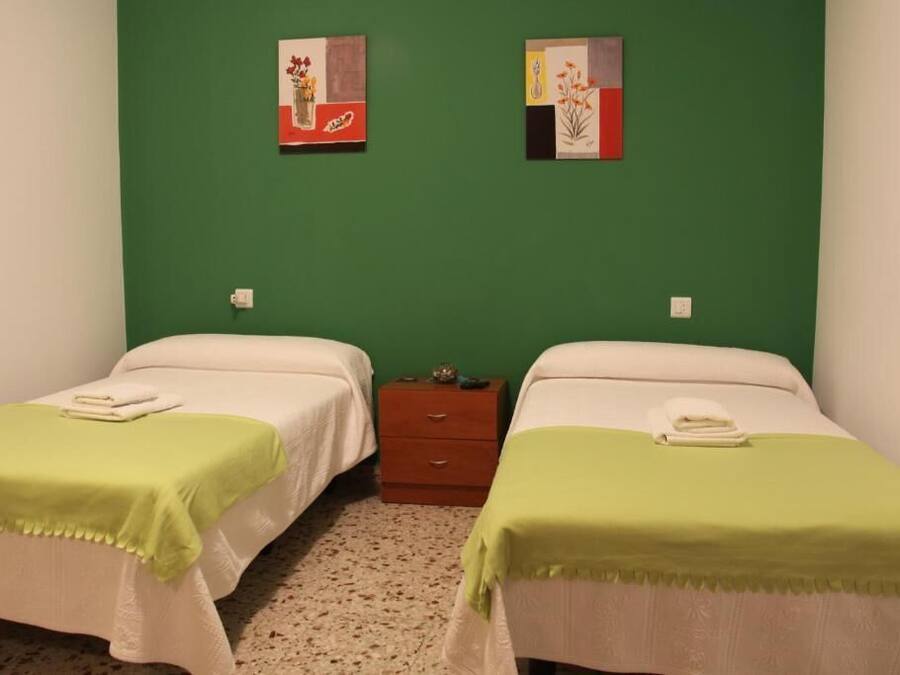 A room with two beds, each with a green blanket and white bedding. There are two paintings on the wall above the beds.