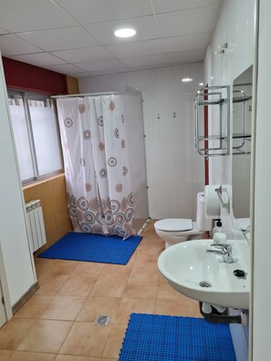 Casa de banho com lavatório branco, sanita e chuveiro com cortina estampada, e um tapete azul.