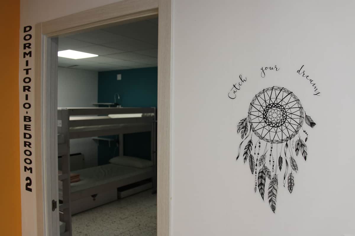 Une chambre de dortoir avec des lits superposés et un mur orné d’une illustration représentant un attrape-rêves.
