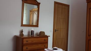 A bedroom with a wooden dresser, a mirror, a door, and a bed with a purple blanket.