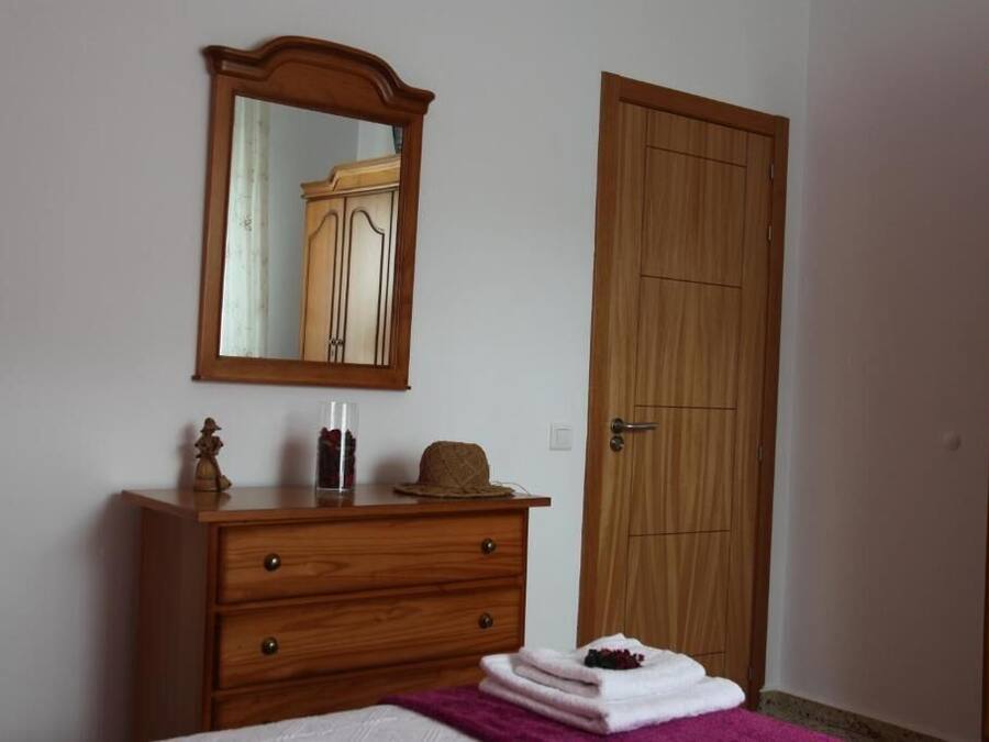 A bedroom with a wooden dresser, a mirror, a door, and a bed with a purple blanket.