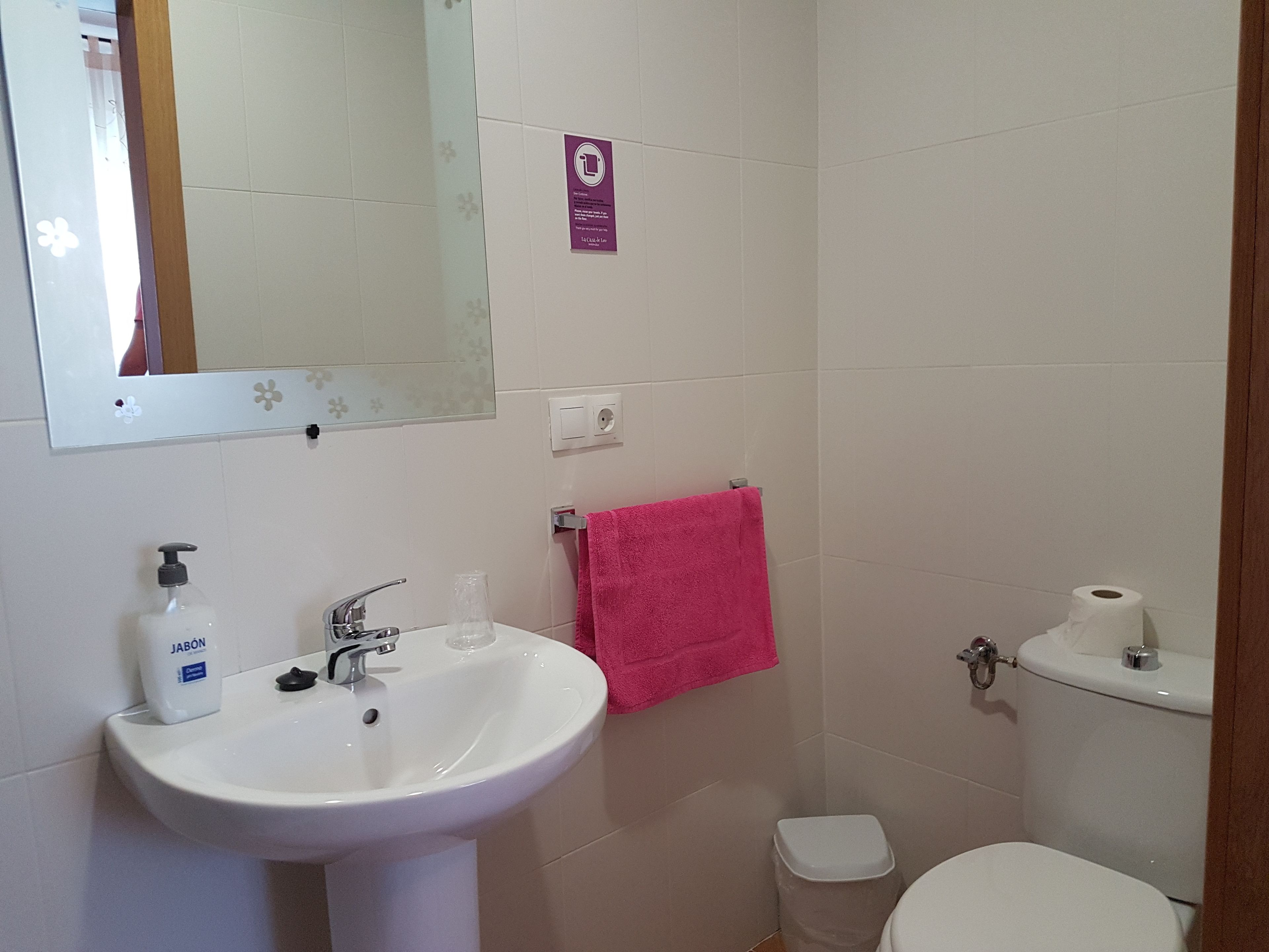 Ein Badezimmer mit einem weißen Waschbecken, einem Spiegel, einem rosafarbenen Handtuch und einer Toilette.