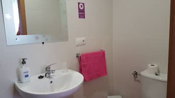 Ein Badezimmer mit einem weißen Waschbecken, einem Spiegel, einem rosafarbenen Handtuch und einer Toilette.