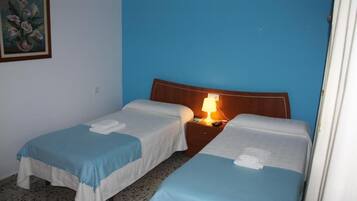 A hotel room with two single beds, a wooden headboard, a nightstand with a lamp, and a painting on the wall.