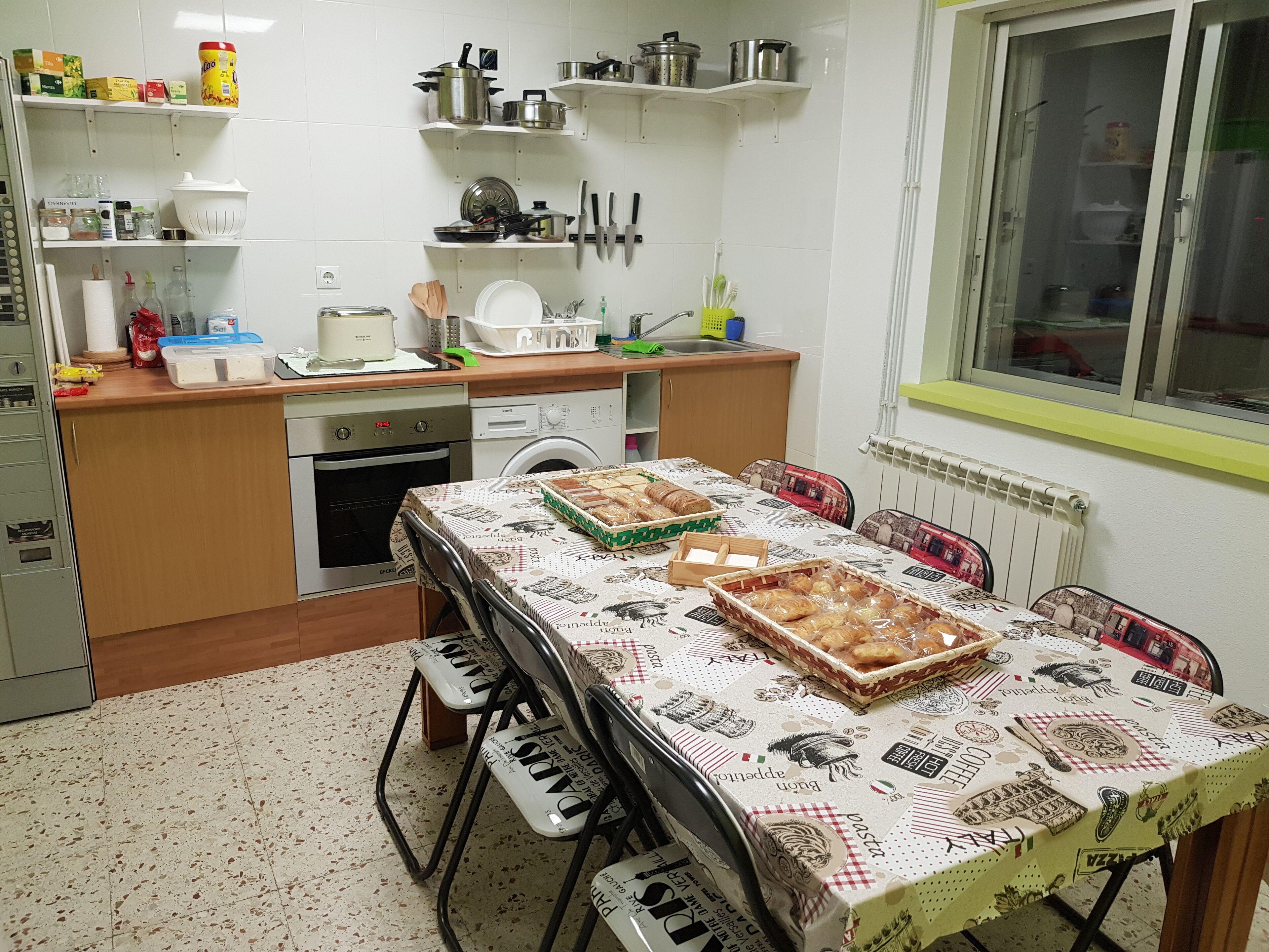Une cuisine compacte avec une table à manger pour deux personnes, agrémentée d’une nappe ornée de motifs liés à la nourriture.