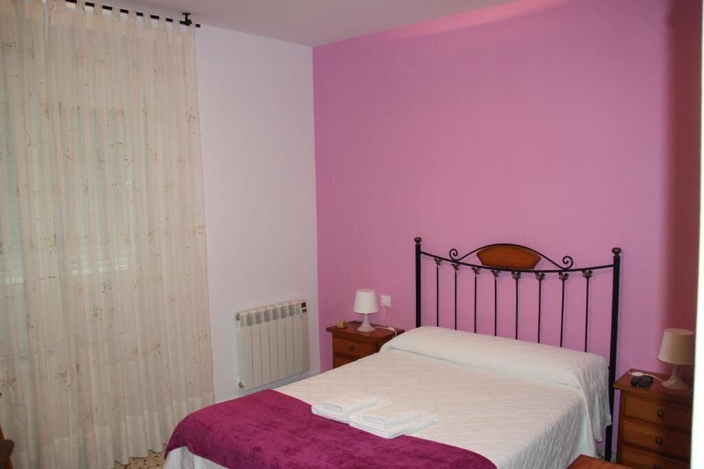 Un dormitorio con una cama, una mesita de noche, una lámpara y una ventana con cortinas.