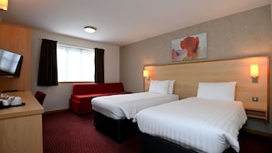 Habitación de hotel con dos camas, un sofá rojo, un escritorio con televisor y una ventana con cortinas.