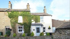 A traditional stone building with a white facade, a small attached structure with a blue door, and a chimney. - Seaton Cottage (Leyburn)