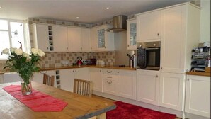 A kitchen with white cabinets, a wooden countertop, a red rug, and a vase with flowers. - Seaton Cottage (Leyburn)