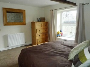 A bedroom with a bed, a dresser, a radiator, a window with curtains, and a hanging toy.