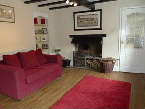 A living room with a red sofa, a fireplace, and a red rug. - Seaton Cottage (Leyburn)