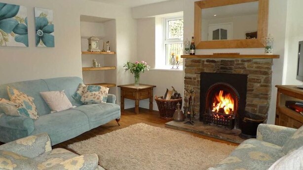 A cozy living room with a fireplace, a blue sofa, and a stone fireplace surround. - Seaton Cottage (Leyburn)