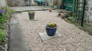A stone courtyard with gravel paths, potted plants, and a green door. - Seaton Cottage (Leyburn)