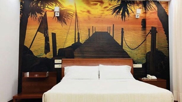A bedroom with a wooden bed, white bedding, and a mural of a sunset over water with palm trees. - Motel Abalo (Catoira)