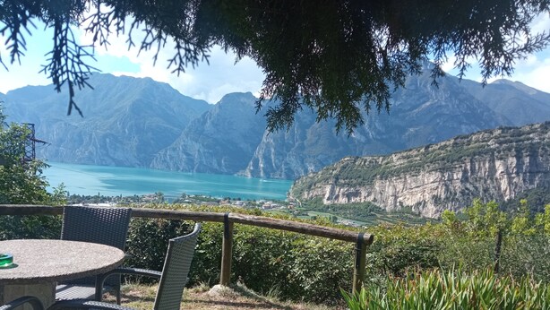 Una terraza con sillas de mimbre y una mesa con vistas a un lago turquesa y montañas.