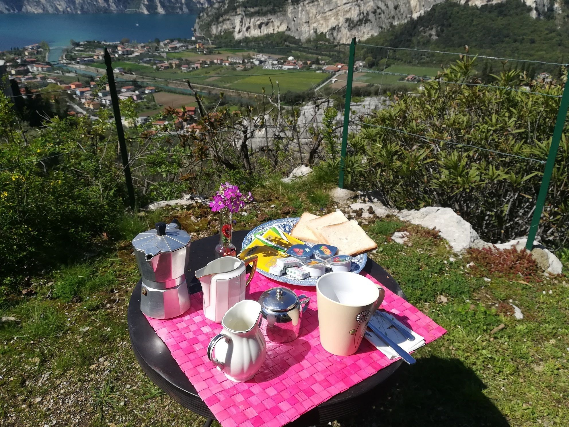 Un montaje para picnic con una mesa, comida y vasos sobre una colina cubierta de hierba, con vistas a un valle pintoresco y la costa.
