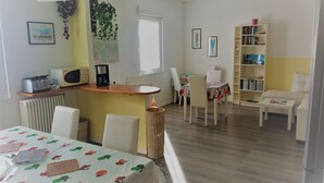 Un comedor con una mesa cubierta por un mantel estampado con motivos de frutas, un microondas y una cafetera en un estante.
