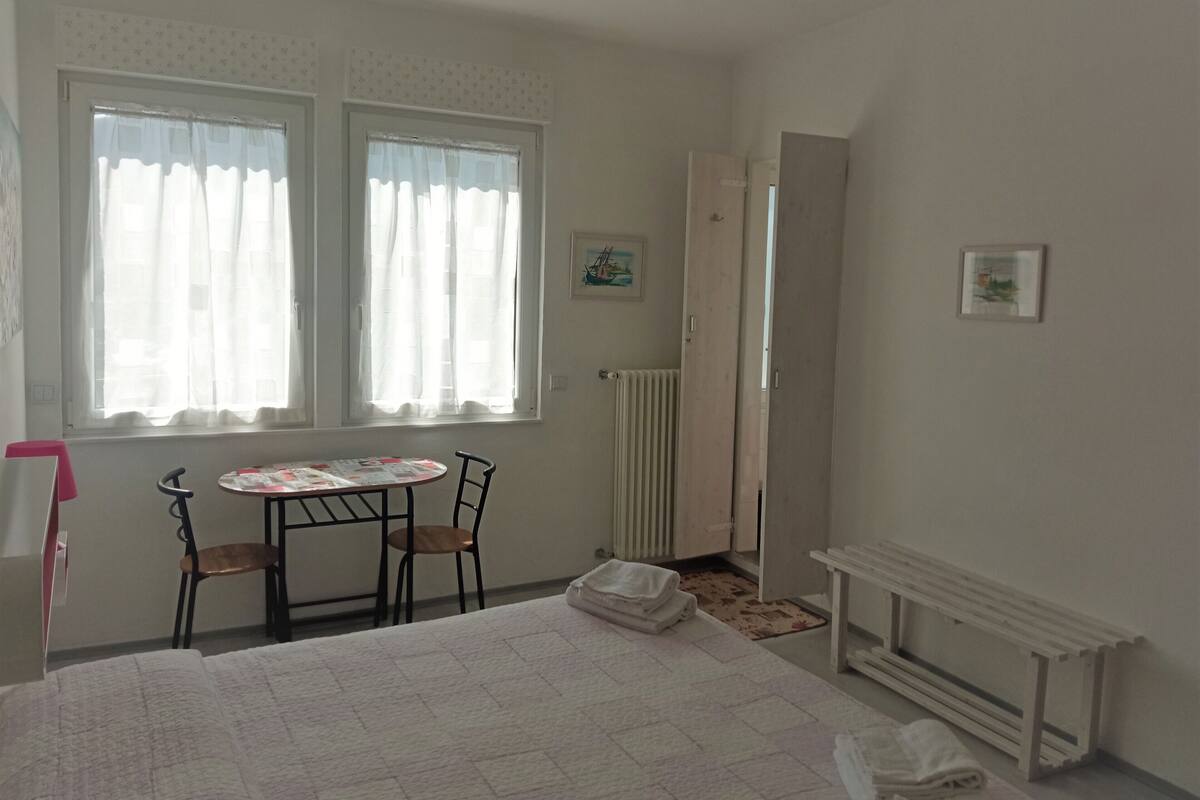 A bedroom with a bed, two chairs, a table, a radiator, and a door.