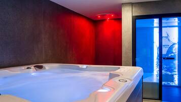 Une salle de spa moderne avec un jacuzzi, des murs rouges et une porte en verre donnant sur un espace piscine.