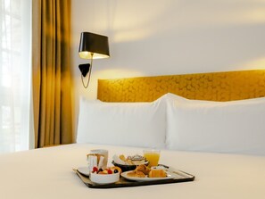 A hotel room with a neatly made bed, a tray with breakfast items, and a wall-mounted lamp. - Hôtel Ginkgo (Quimper)