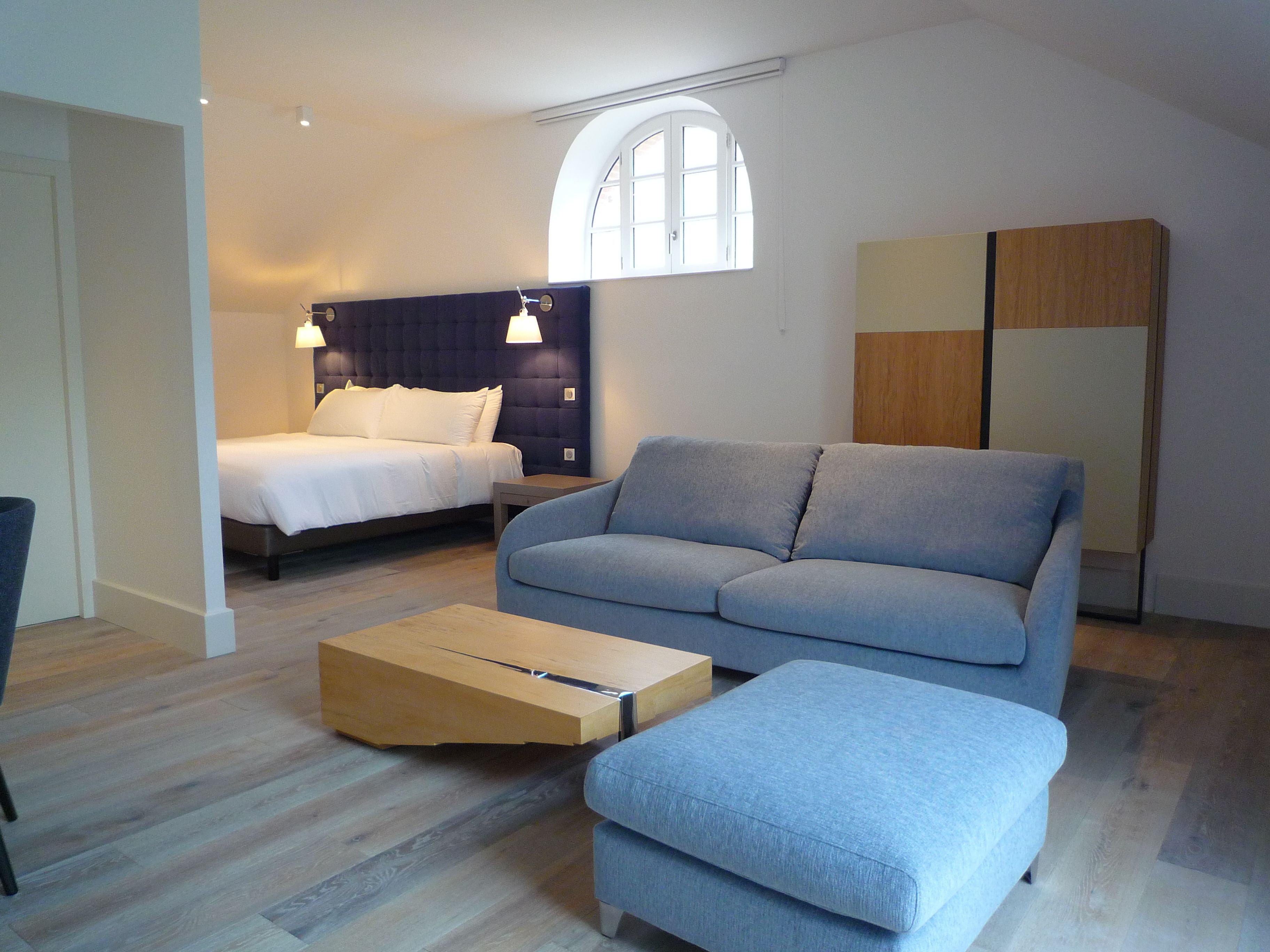 A modern bedroom with a bed, a sofa, a wooden side table, and a wardrobe.