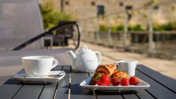 Une table avec une théière, des tasses, une assiette de fraises et de croissants, et une chaise.