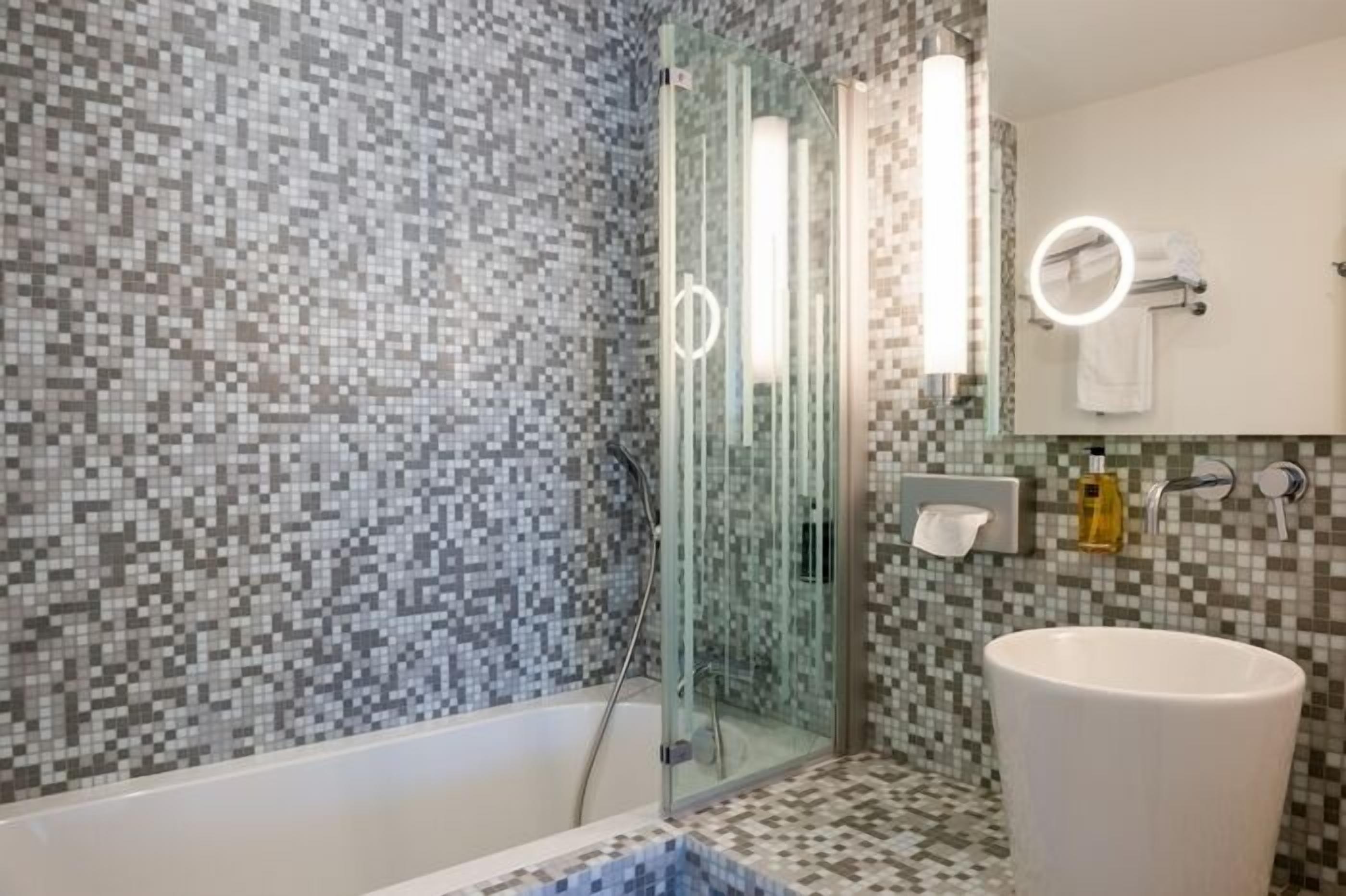 Un baño con cabina de ducha de vidrio, un lavamanos blanco y un salpicadero de azulejos.
