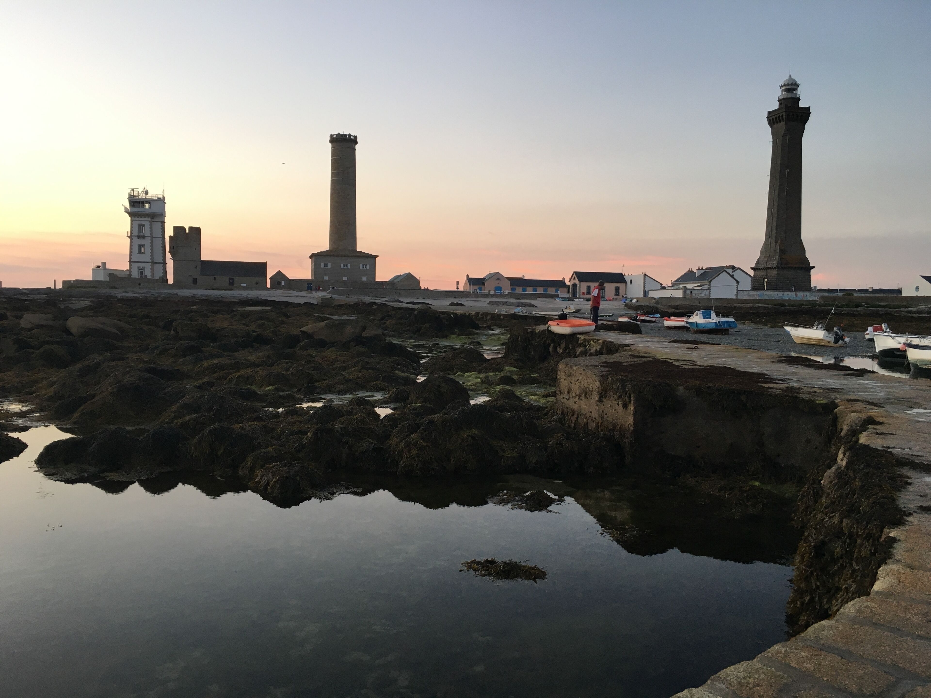 A coastal scene with a lighthouse, rocky shore, and calm water reflecting the structures.