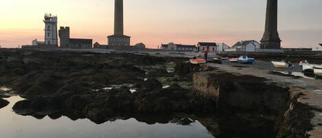 A coastal scene with a lighthouse, rocky shore, and calm water reflecting the structures.