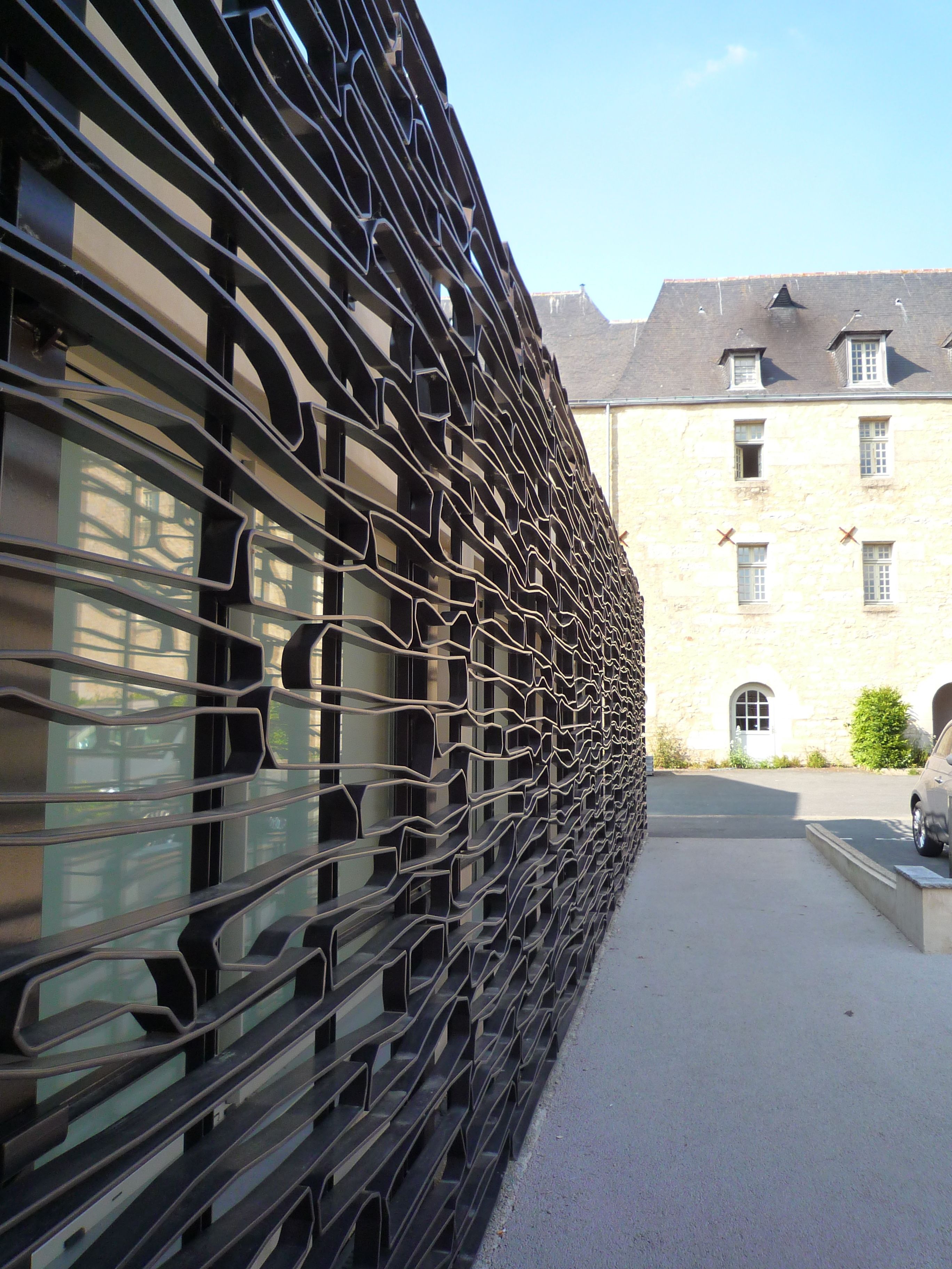 A building with a unique black metal facade and a stone building in the background.