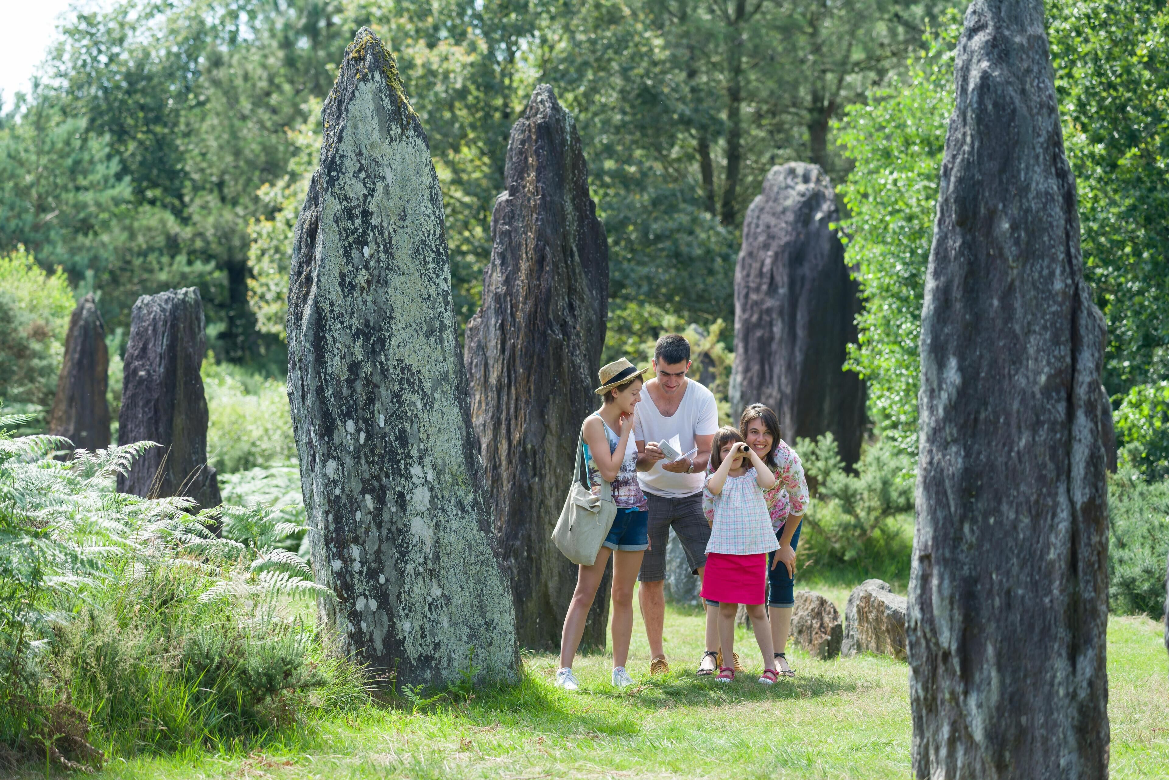 Eine Familie steht in bewaldeter Landschaft in der Nähe hoher, natürlicher Felsformationen.