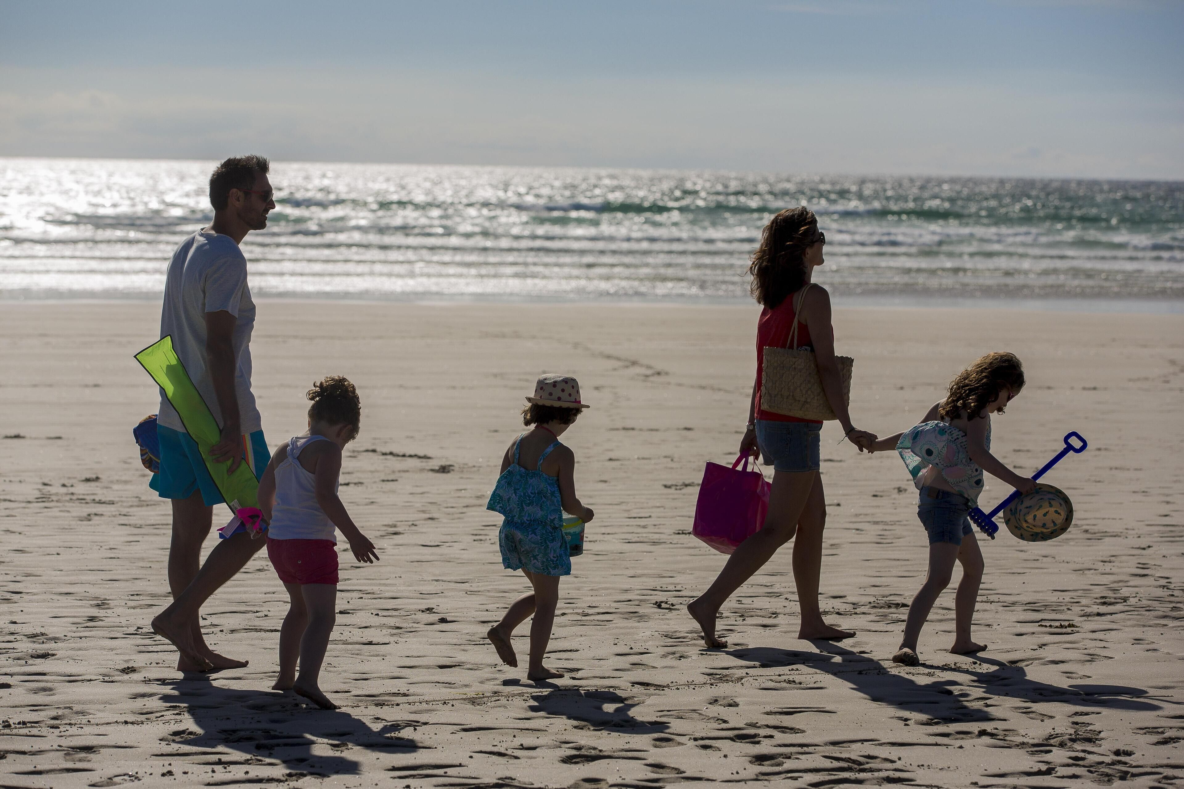 Une famille se promène sur une plage de sable, avec l’océan en arrière-plan.