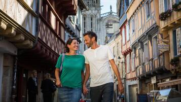 A couple walking on a narrow street with historic buildings, including a cathedral in the background.