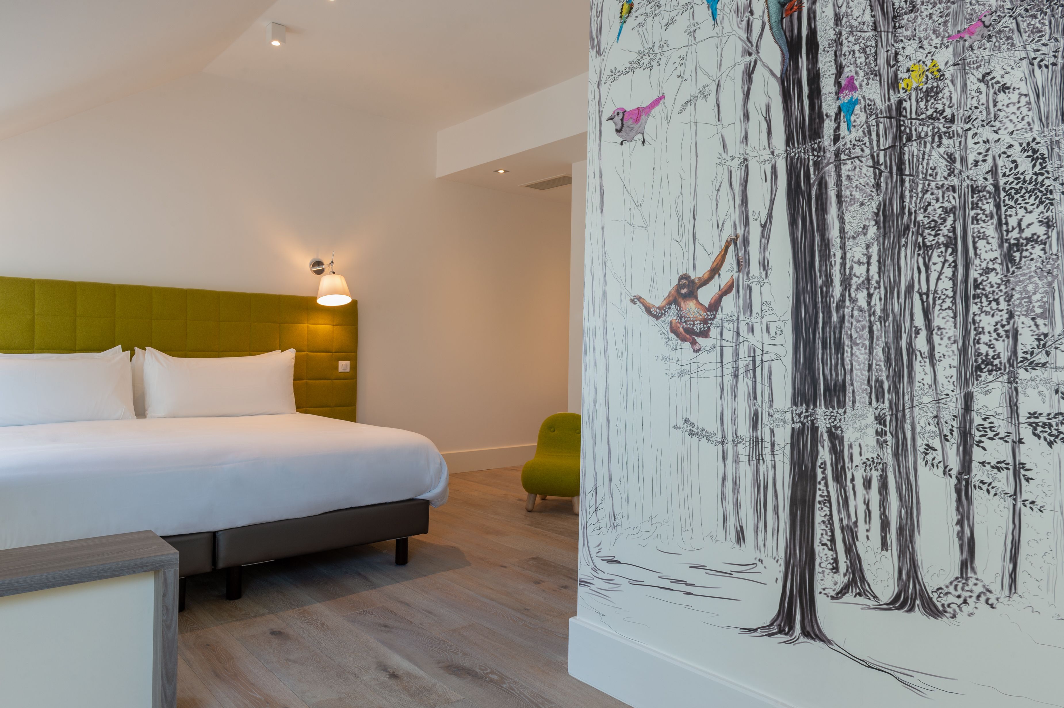 Une chambre à coucher avec un lit, une tête de lit verte, une fresque murale et une chaise verte.