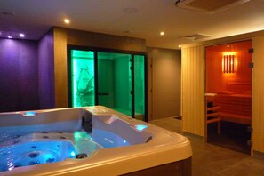 A spa room with a hot tub, a wooden door leading to a sauna, and a green-lit glass door. - Hôtel Ginkgo (Quimper)