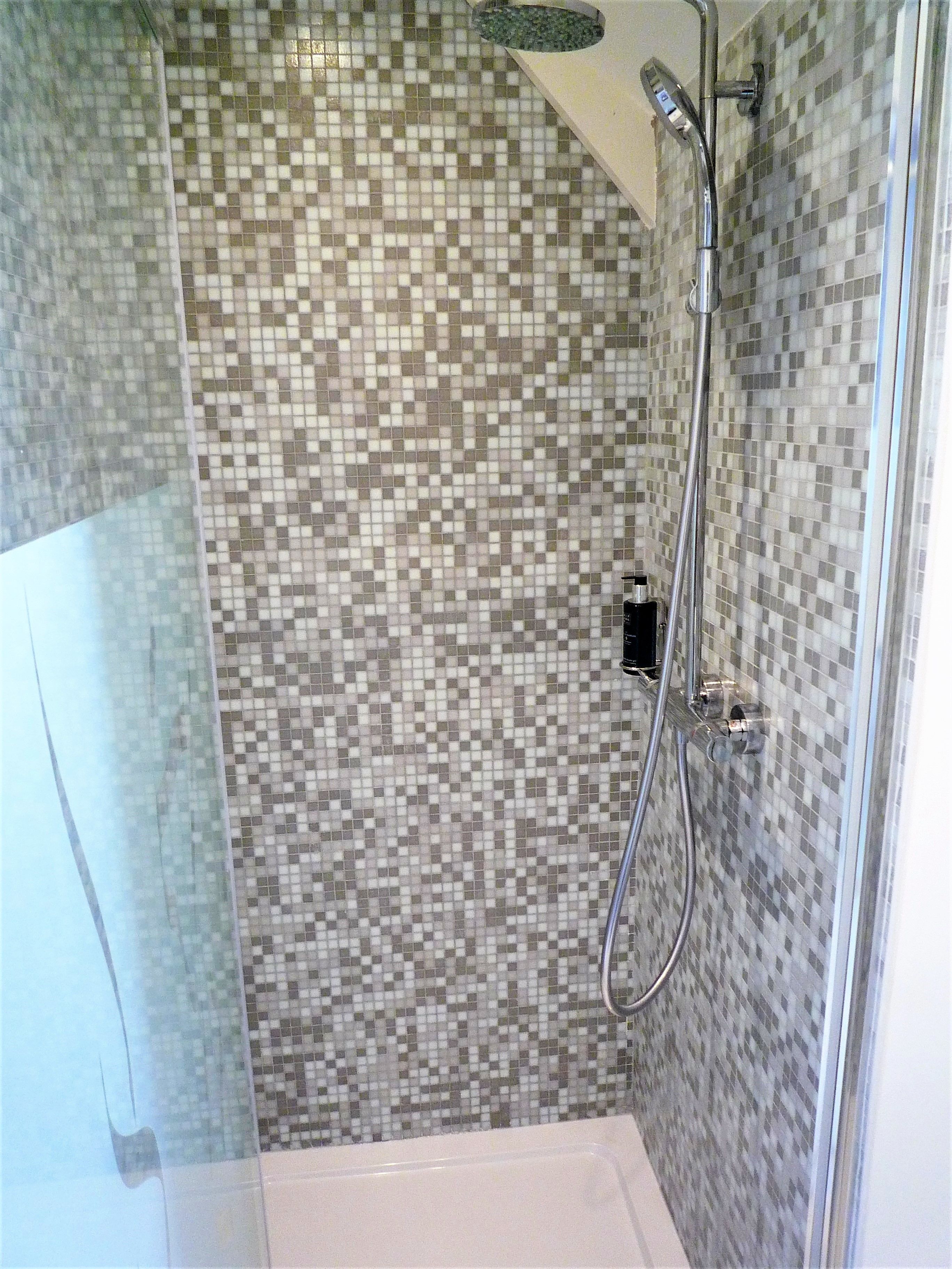 Una ducha con pared de mosaico de azulejos, un cabezal de ducha de mano y un grifo empotrado.