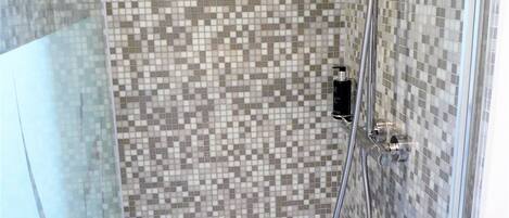 Una ducha con pared de mosaico de azulejos, un cabezal de ducha de mano y un grifo empotrado.