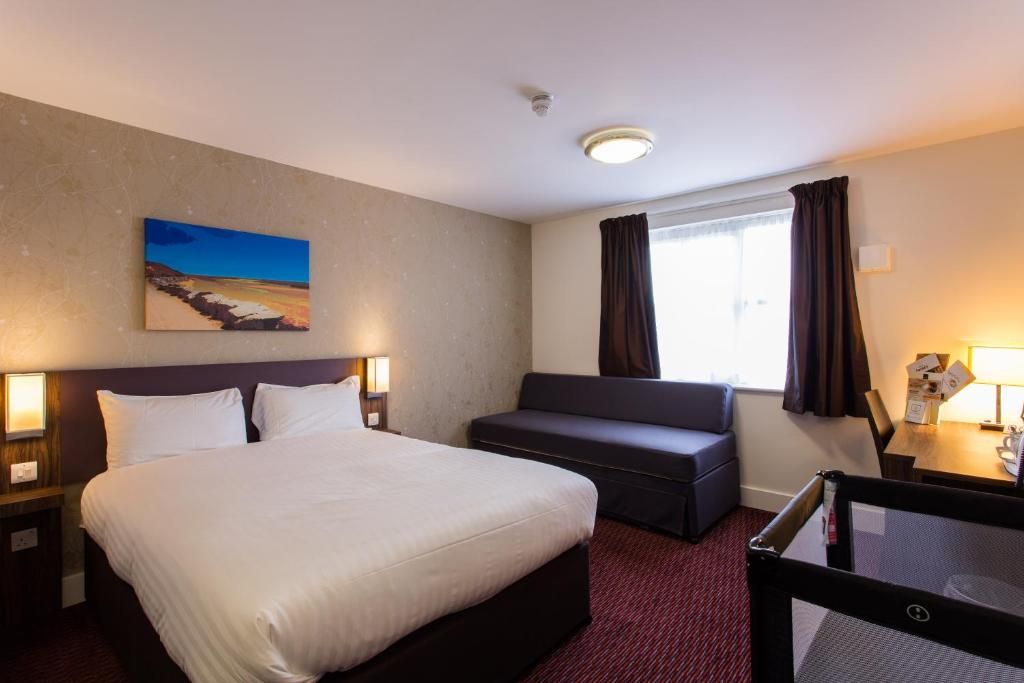 A hotel room with a bed, a seating area, a window with curtains, and a painting on the wall.