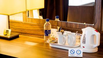 A hotel room's reception area with a wooden counter, a water bottle, coffee cups, a tea kettle, and a sign indicating free Wi-Fi and no smoking.