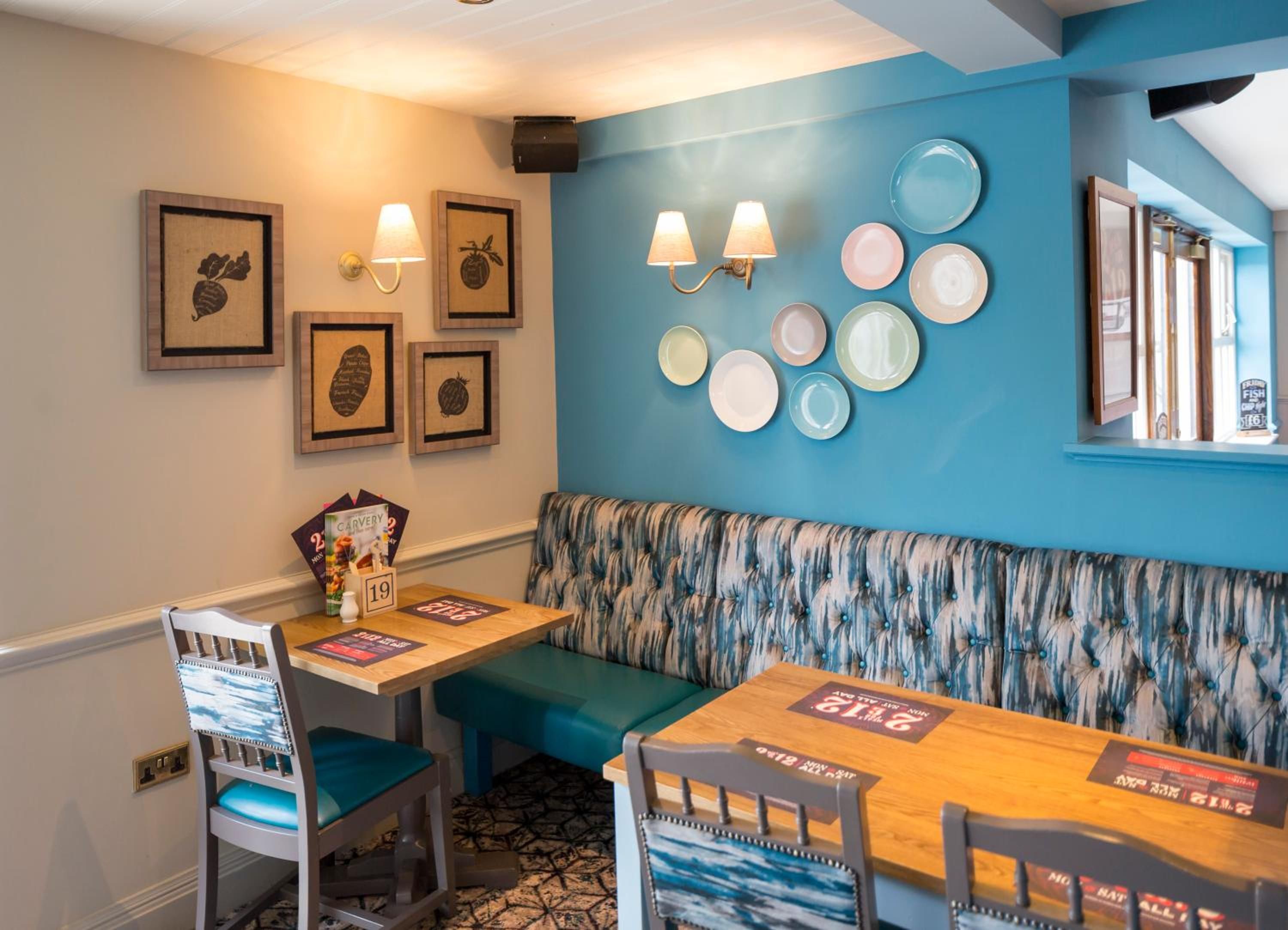 A restaurant interior with a blue wall, framed artwork, wall-mounted lights, and a patterned bench.