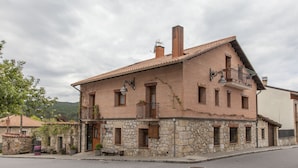 A two-story stone building with a tiled roof, a balcony with a wrought iron railing, and a small attached stone structure with a wooden door. - La Casona del Herrero (Navaleno)