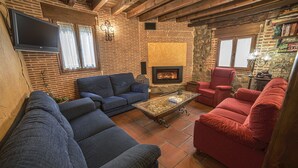 A cozy living room with a fireplace, blue and red sofas, and a flat-screen TV mounted on the wall. - La Casona del Herrero (Navaleno)