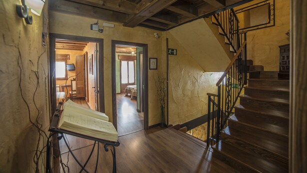 A wooden staircase with a metal railing, a hallway with wooden floors, and a door leading to another room. - La Casona del Herrero (Navaleno)