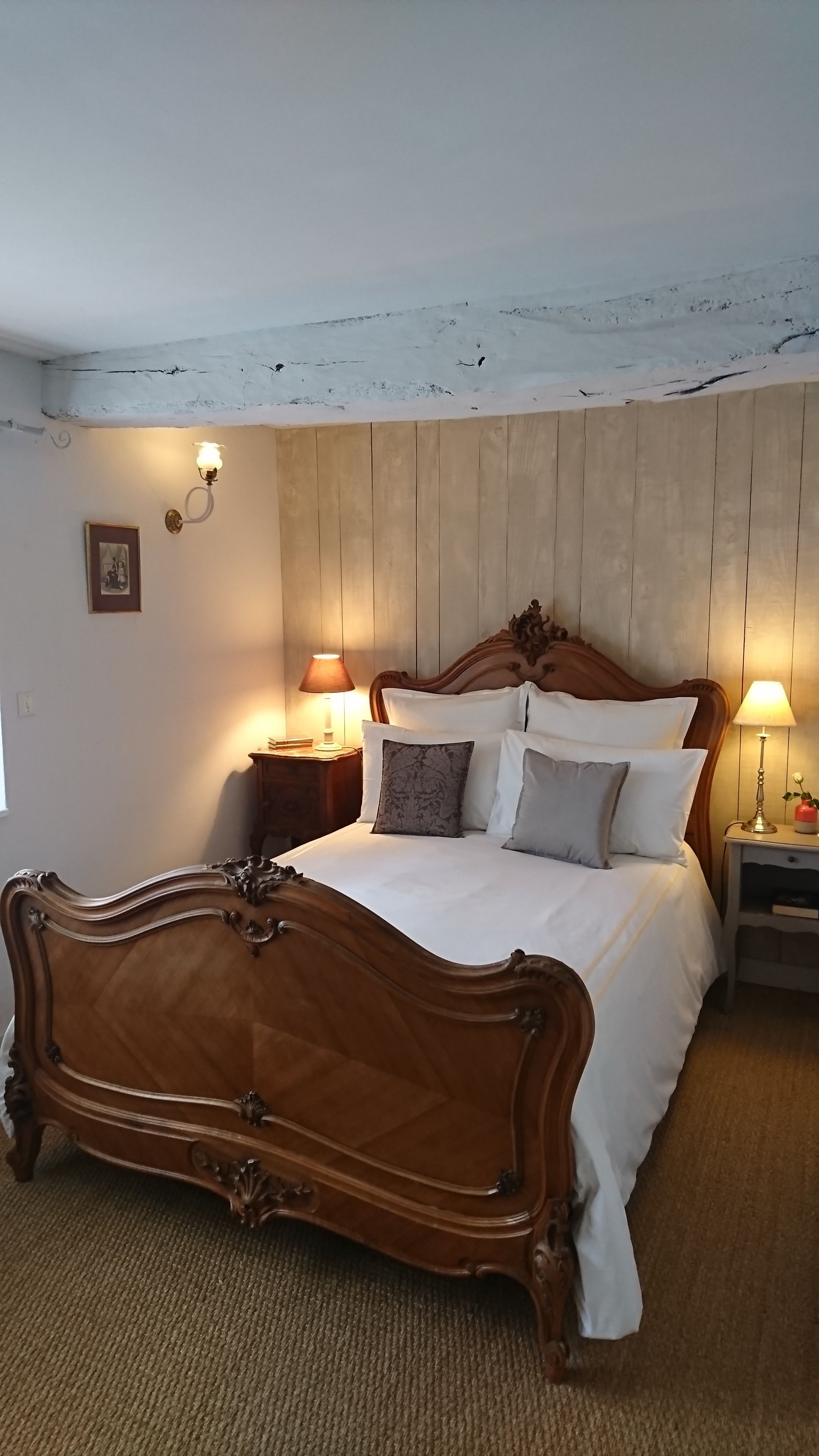 Une chambre à coucher avec un lit en bois, deux tables de chevet avec des lampes, une tête de lit en bois et un tableau au mur.